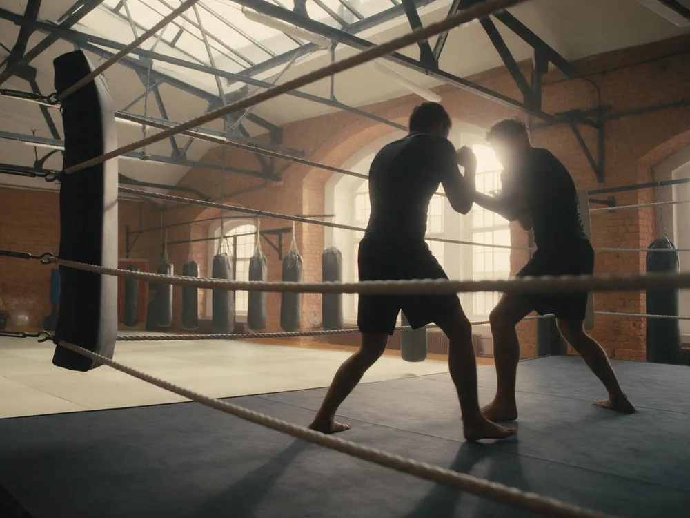 Due figure si allenano sul ring, riprese da fuori attraverso le corde.